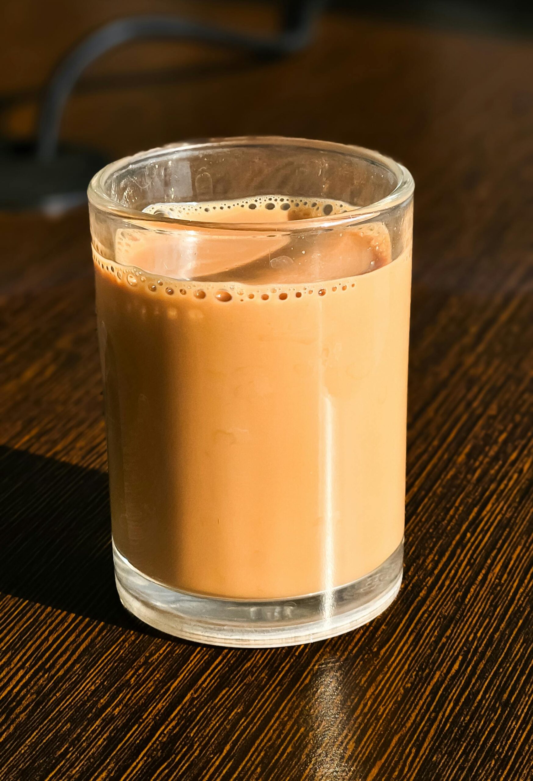 Close-up of a glass filled with creamy Indian masala chai on a wooden table.